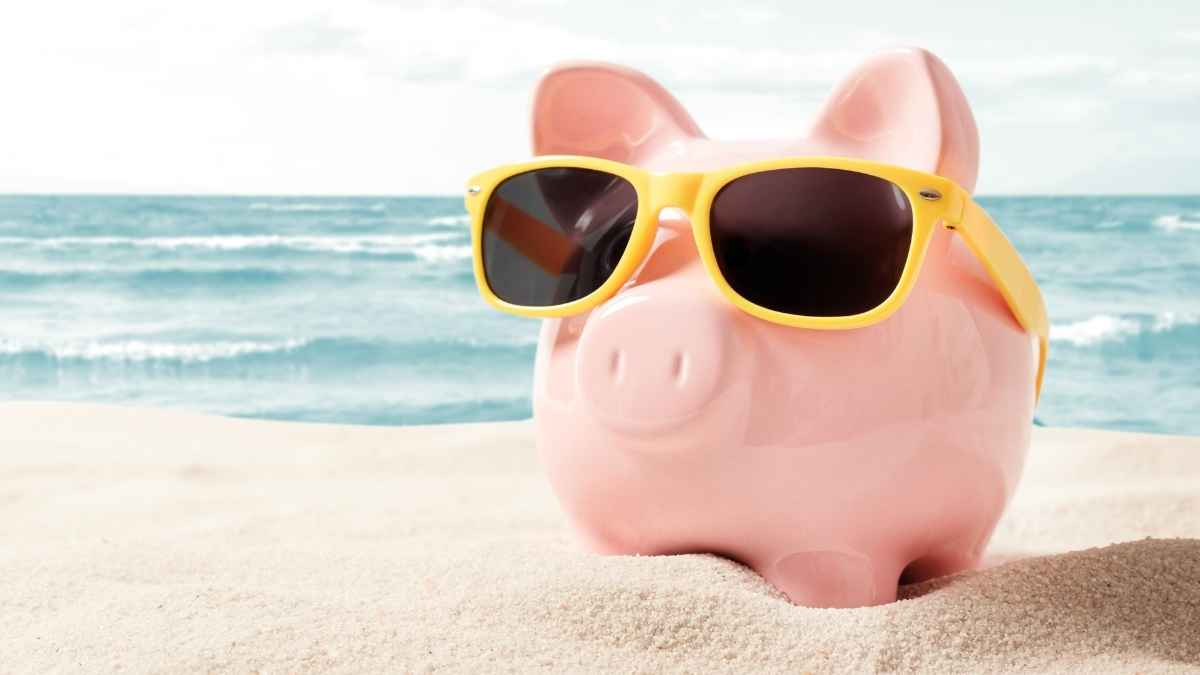 Hucha con gafas de sol en la playa simbolizando las vacaciones como gasto fijo para evitar endeudarse