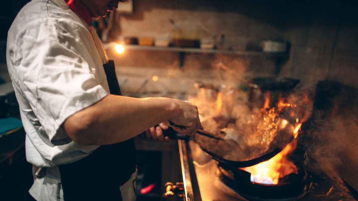 Cocinero en primer plano trabajando con sartén al fuego en la cocina de un restaurante