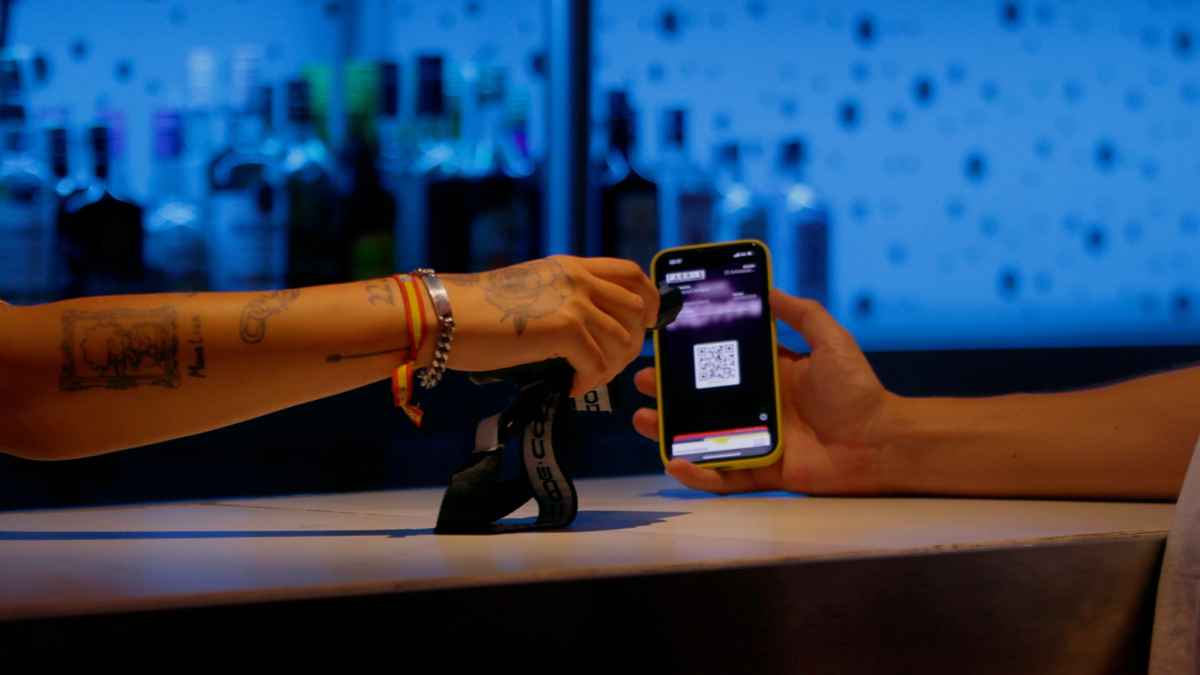 Escaneo de código QR en barra de discoteca de Ibiza; manos de camarera y cliente