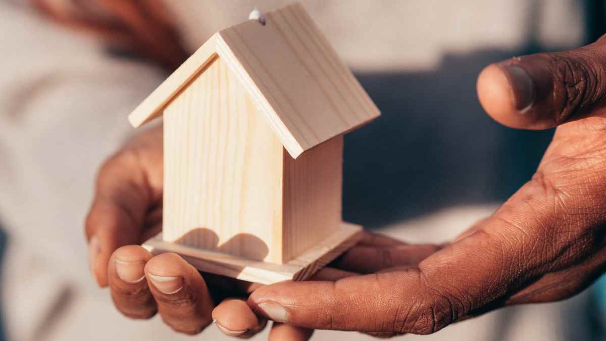 Manos sosteniendo una casa de madera, símbolo de herencia de vivienda entre hijos y riesgos de la copropiedad