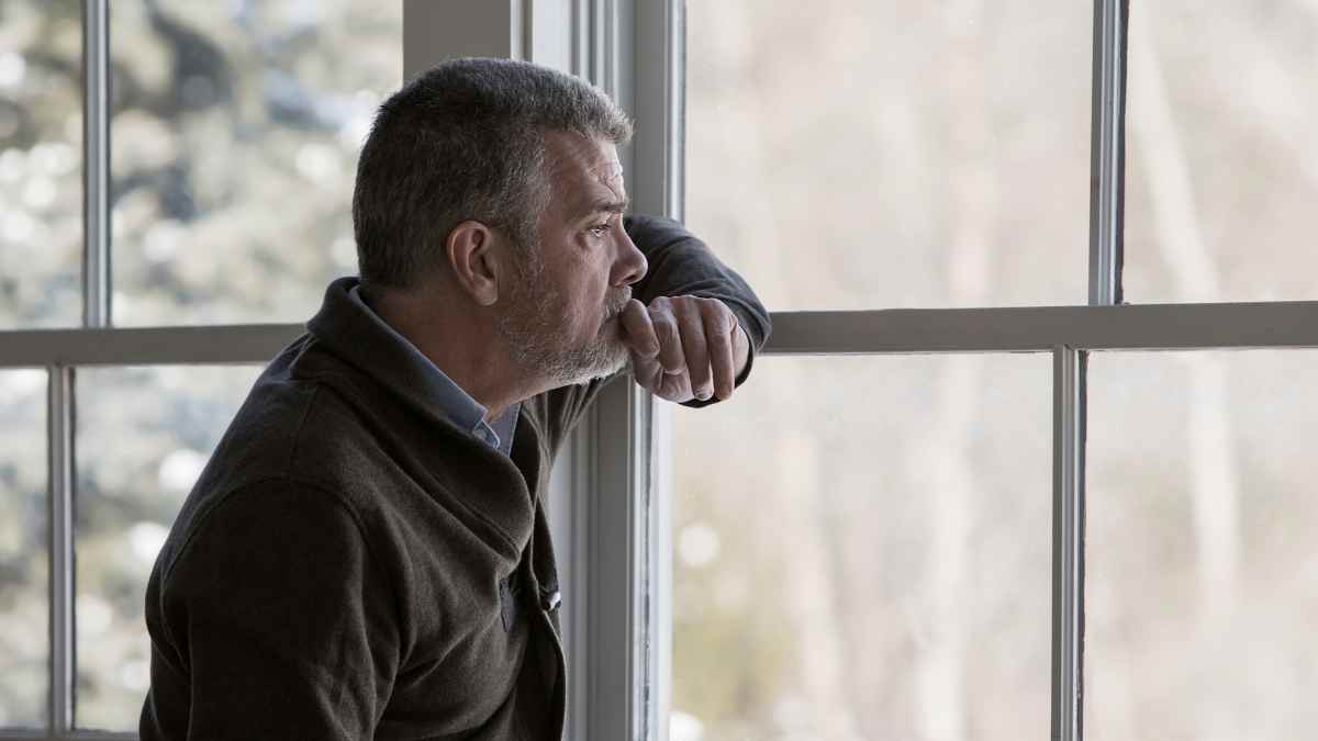 Jubilado pensativo mirando por la ventana tras pedir un anticipo de 100 euros y firmar un seguro de hogar de tres años