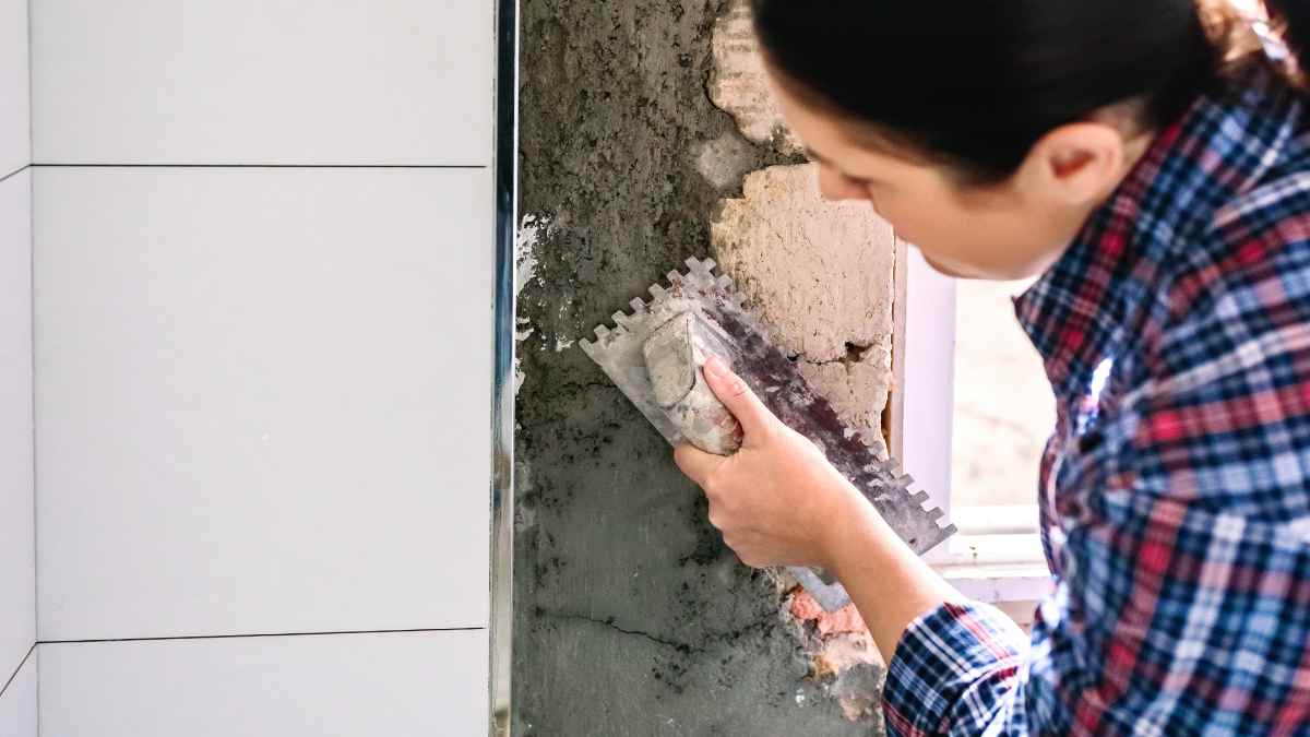Albañila alicatando una pared con llana dentada durante una reforma de obra