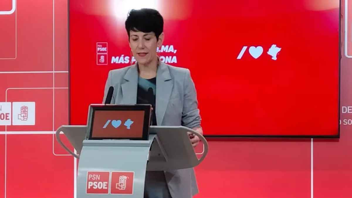 Portavoz en el atril del PSN-PSOE durante rueda de prensa, fondo rojo, permiso por donación con sueldo al 100%