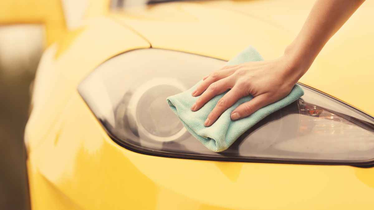 Persona limpiando el faro opaco de un coche amarillo con un producto de Mercadona