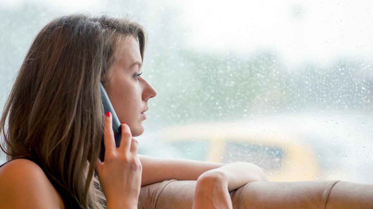 Mujer al teléfono mirando por la ventana en un día de lluvia, imagen sobre spam telefónico y Lista Robinson en España