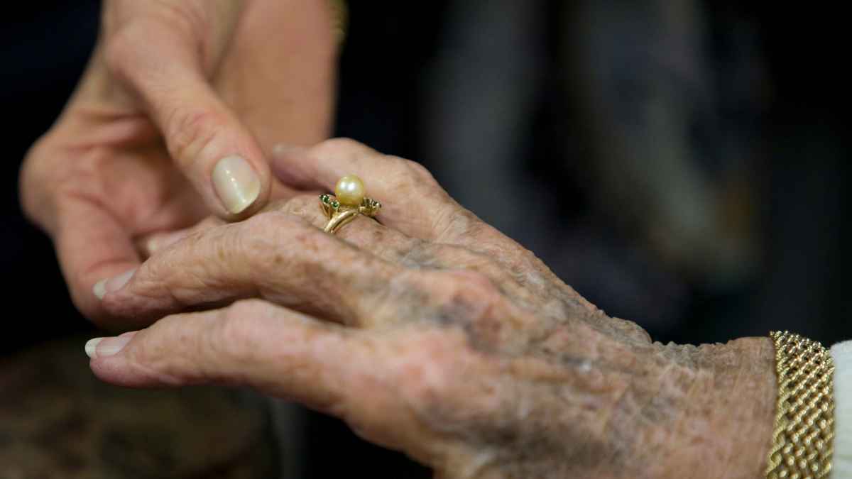 Manos de una persona mayor con anillo de oro con perla y pulsera; joyas heredadas preparadas para tasación.
