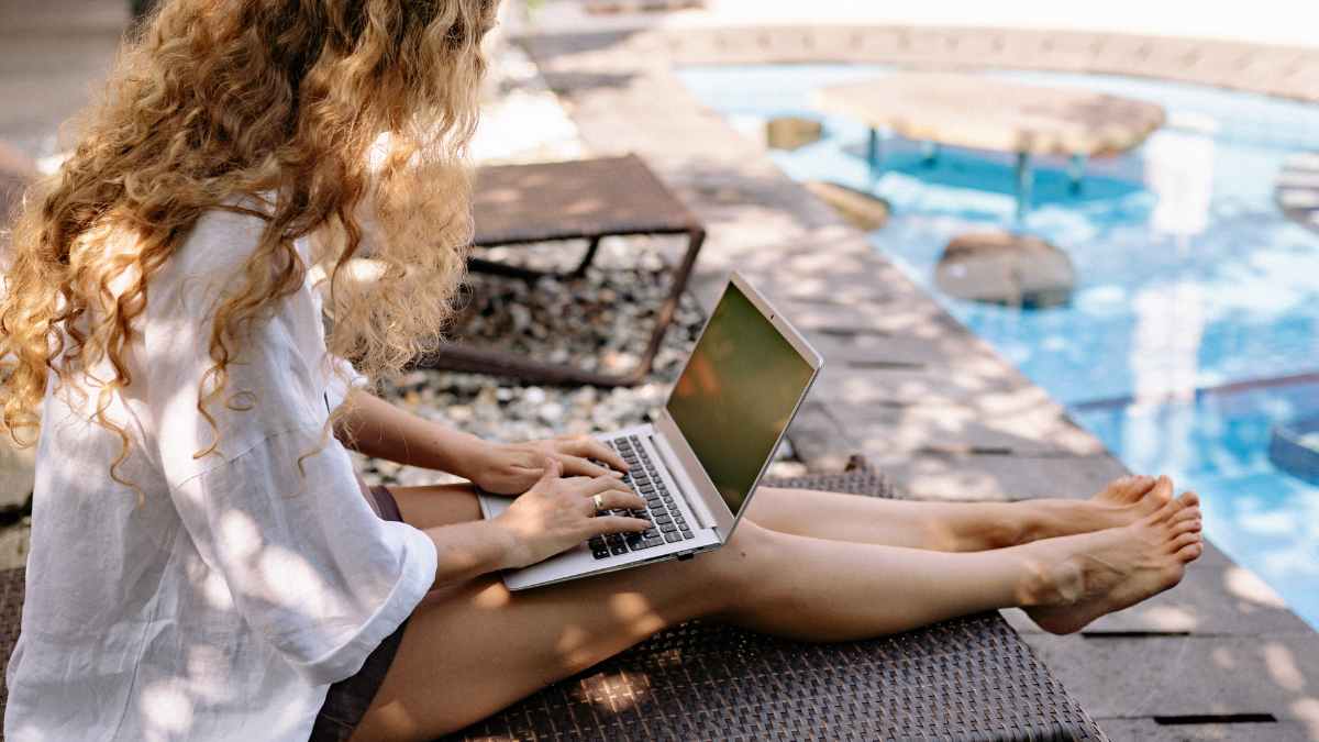 Autónoma trabajando con el portátil junto a la piscina durante sus vacaciones de verano
