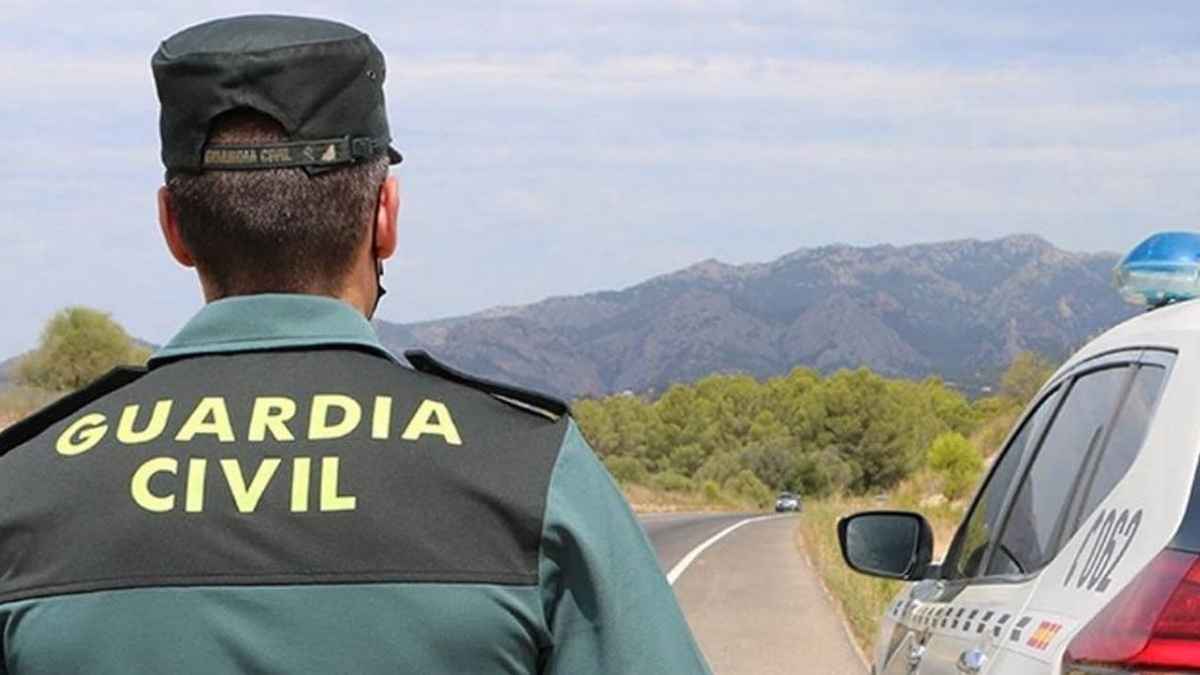 Agente de la Guardia Civil junto a coche patrulla en carretera de montaña