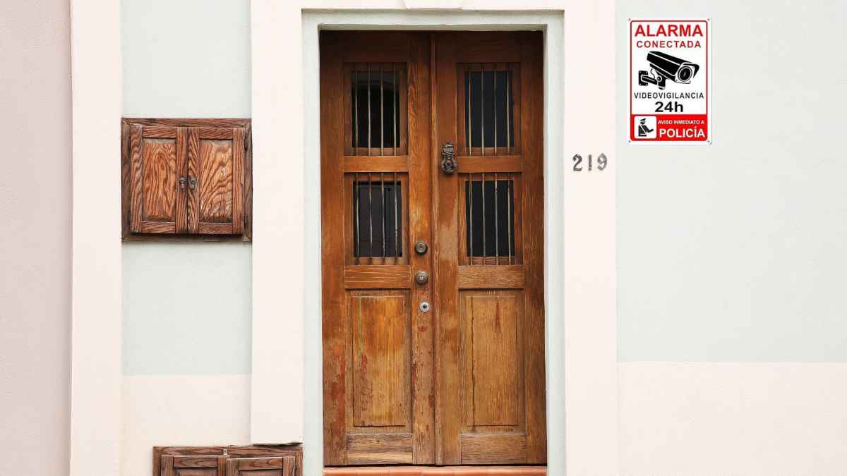 Puerta de vivienda con cartel de alarma conectada sin contrato visible en fachada