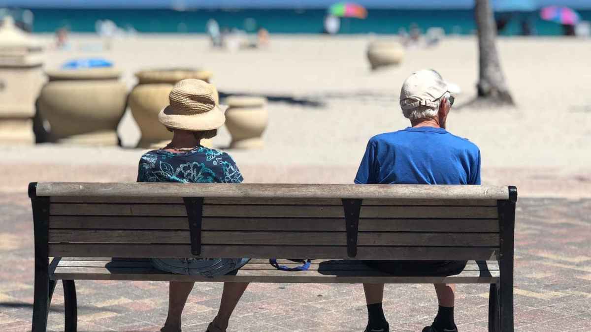 Pareja de pensionistas extranjeros sentados en un banco frente al mar en España
