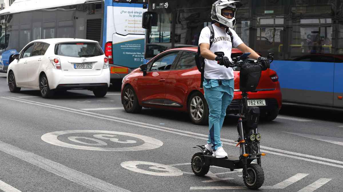 Conductor en patinete eléctrico circulando por ciudad con casco tras la obligación de seguro publicada en el BOE