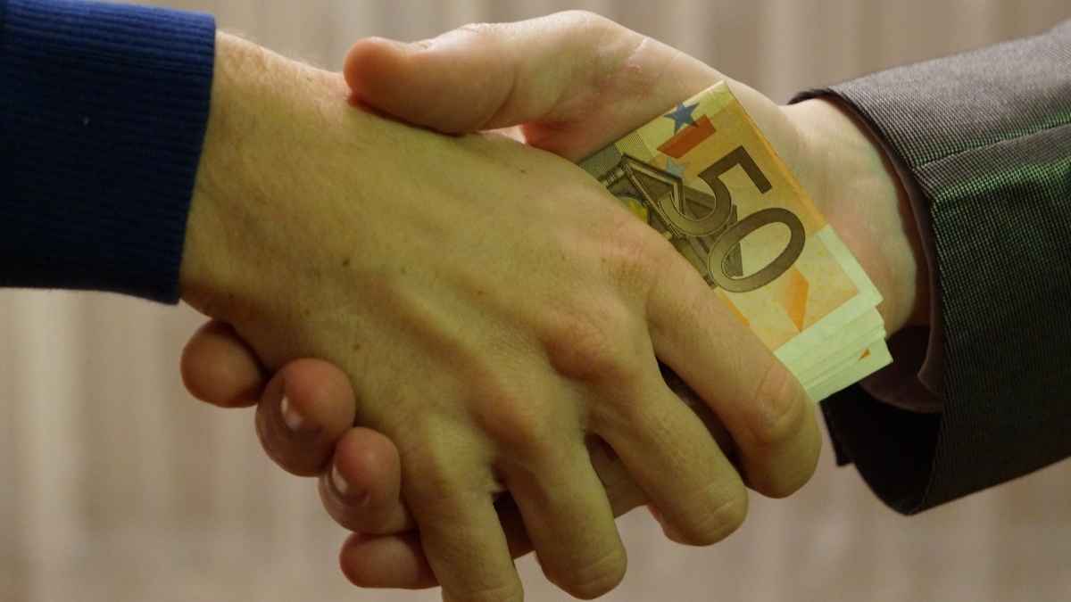 Manos estrechándose con billetes de 50 euros en referencia a ayuda del SEPE de 600 euros durante 120 días