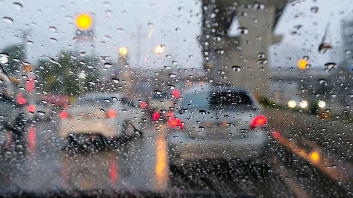 Vista desde el interior de un coche bajo la lluvia con tráfico y luces encendidas, aviso de la DGT sobre multas por descuidos al volante.