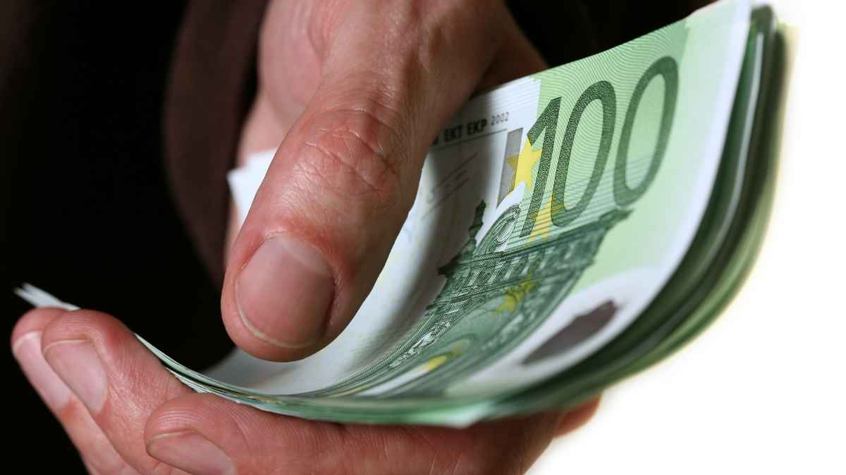 Mano entregando billetes de 100 euros representando la pensión de alimentos extinguida por decisión judicial