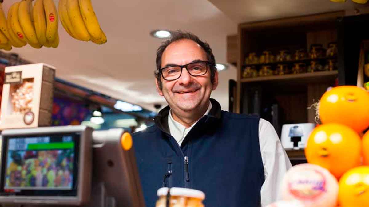 Frutero con 40 años de experiencia atendiendo su puesto en un mercado local con frutas y productos frescos