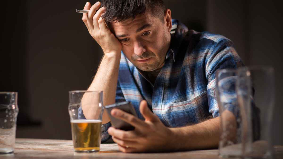 Hombre preocupado con vaso de cerveza revisando su móvil relacionado con pensión por alcoholismo e incapacidad permanente