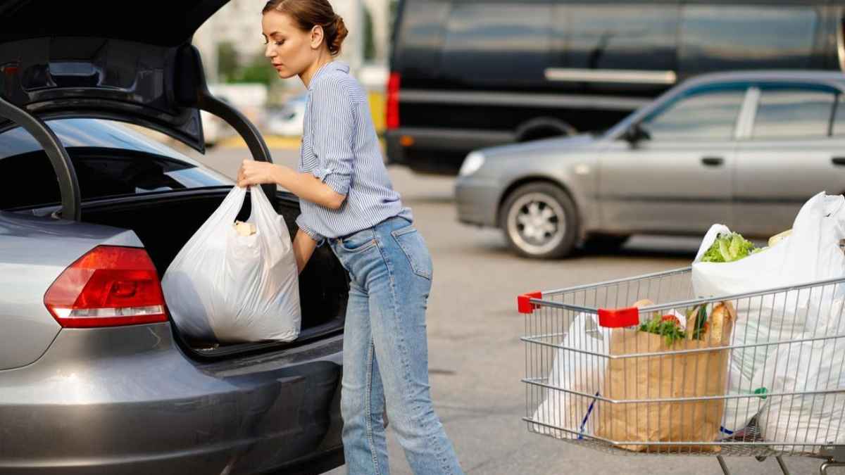 Mujer guardando bolsas de la compra en el maletero del coche tras salir del supermercado, posible multa de la DGT