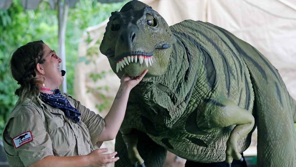 Guía del parque de dinosaurios interactuando con figura animatrónica antes del cierre y venta en Nueva Jersey