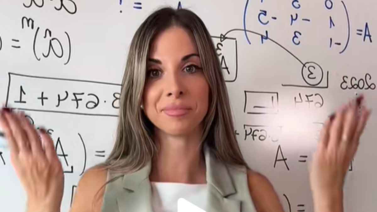 profesora de matemáticas explicando en clase con una pizarra llena de fórmulas