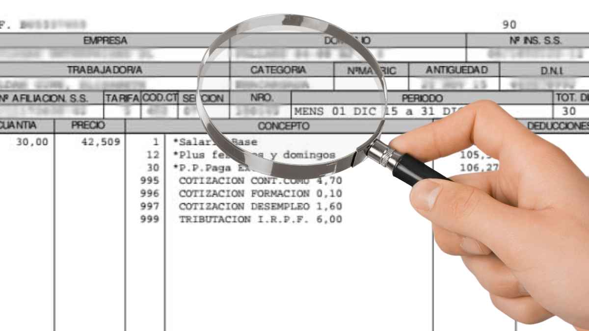 Mano sosteniendo una lupa revisando una nómina para comprobar los devengos y cálculos salariales