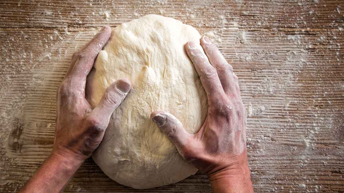 Manos trabajando una masa de pan sobre una mesa enharinada