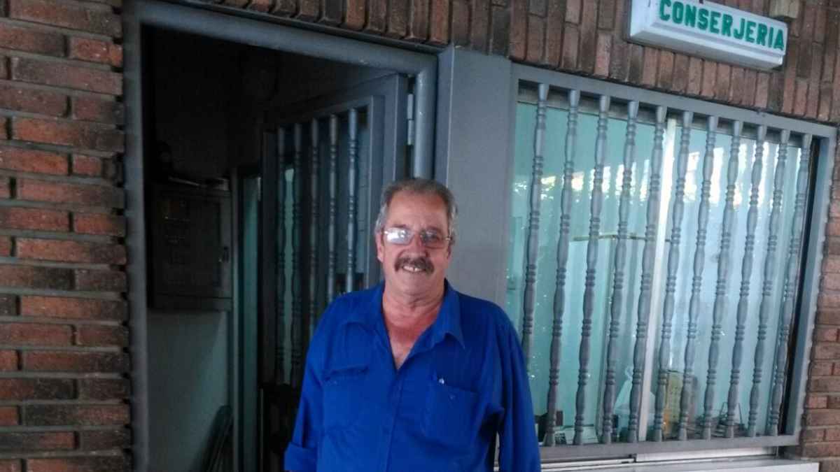 Conserje frente a la entrada de una conserjería con cartel identificativo en un edificio