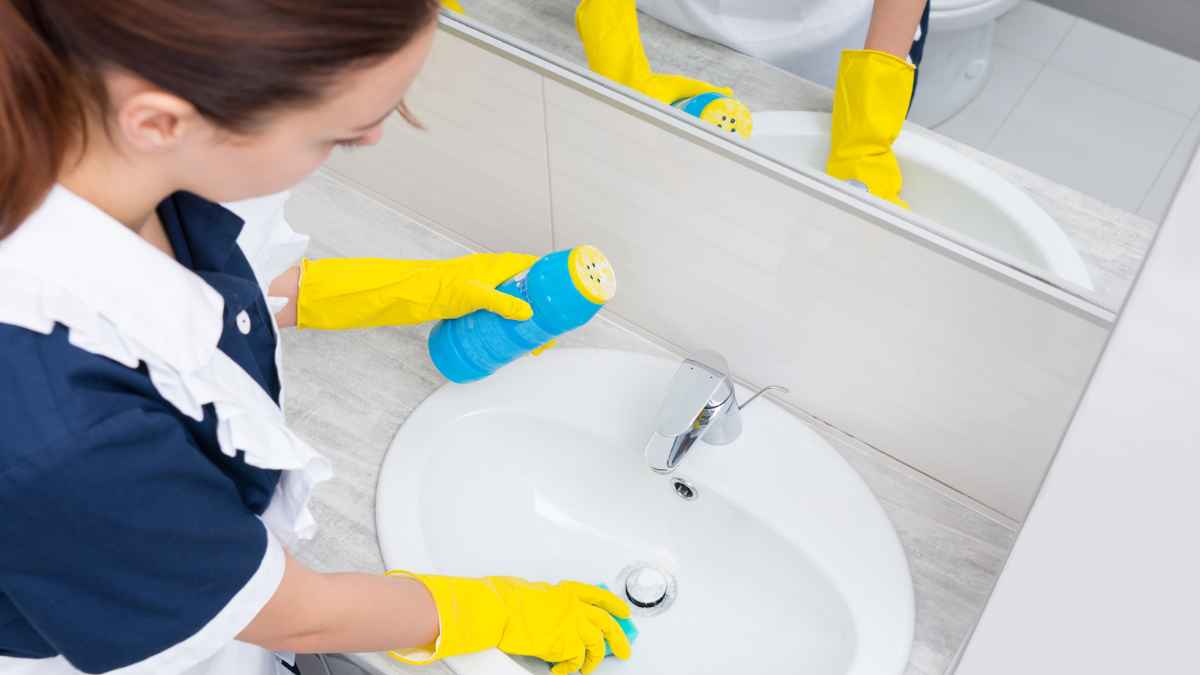 Empleada del hogar limpiando un baño con guantes y productos de limpieza
