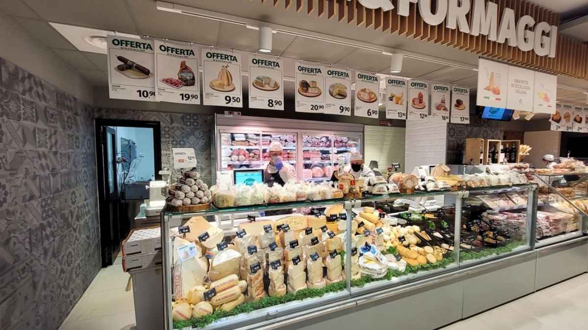 Mostrador de charcutería y quesos en un supermercado con productos en oferta y personal atendiendo tras el mostrador.