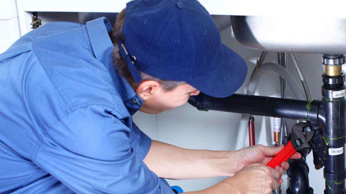 Fontanero arreglando una tubería doméstica mientras explica por qué cobra 200 euros por un trabajo de diez minutos