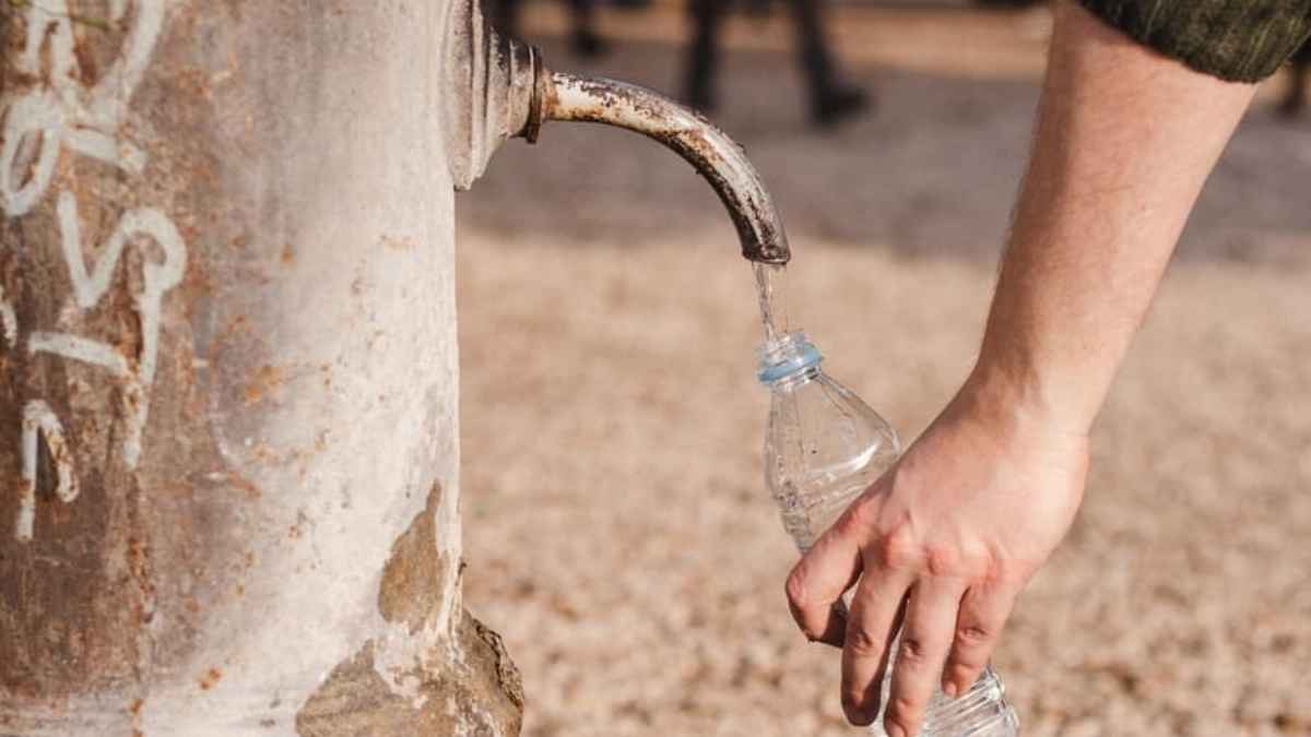 Mano rellenando una botella de plástico con agua en una fuente pública antigua