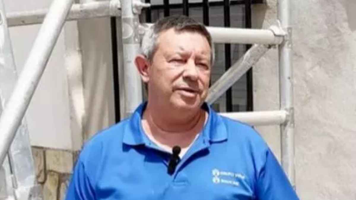 Hombre de mediana edad trabajando en una obra con ropa de trabajo azul delante de una fachada en rehabilitación.