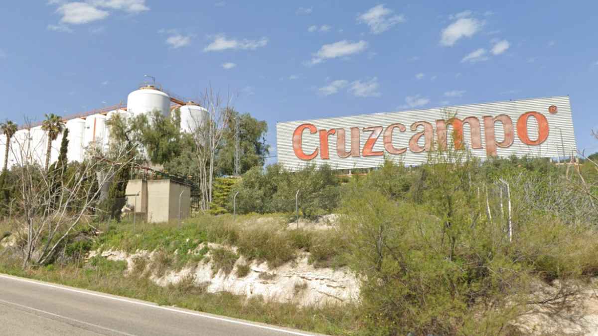 Fábrica de Cruzcampo en Sevilla con depósitos industriales y cartel de la marca visto desde la carretera