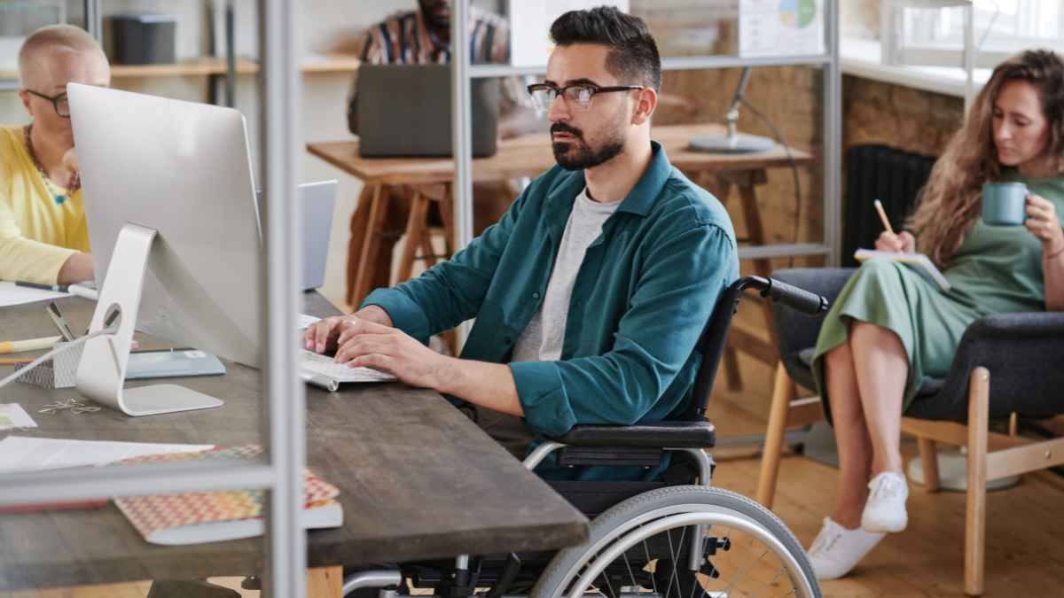 Hombre en silla de ruedas trabajando en oficina representa a las personas con discapacidad que pueden jubilarse anticipadamente a los 52 años en España.