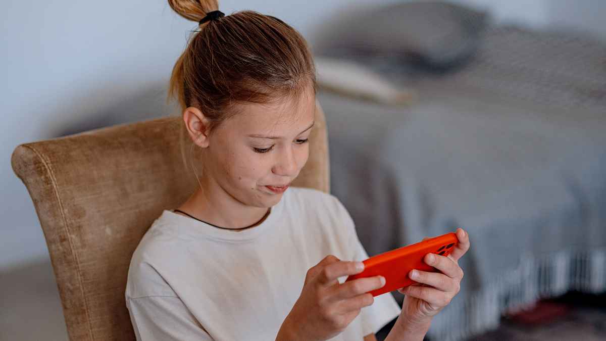 Niña usando un teléfono móvil en una habitación mientras mira la pantalla