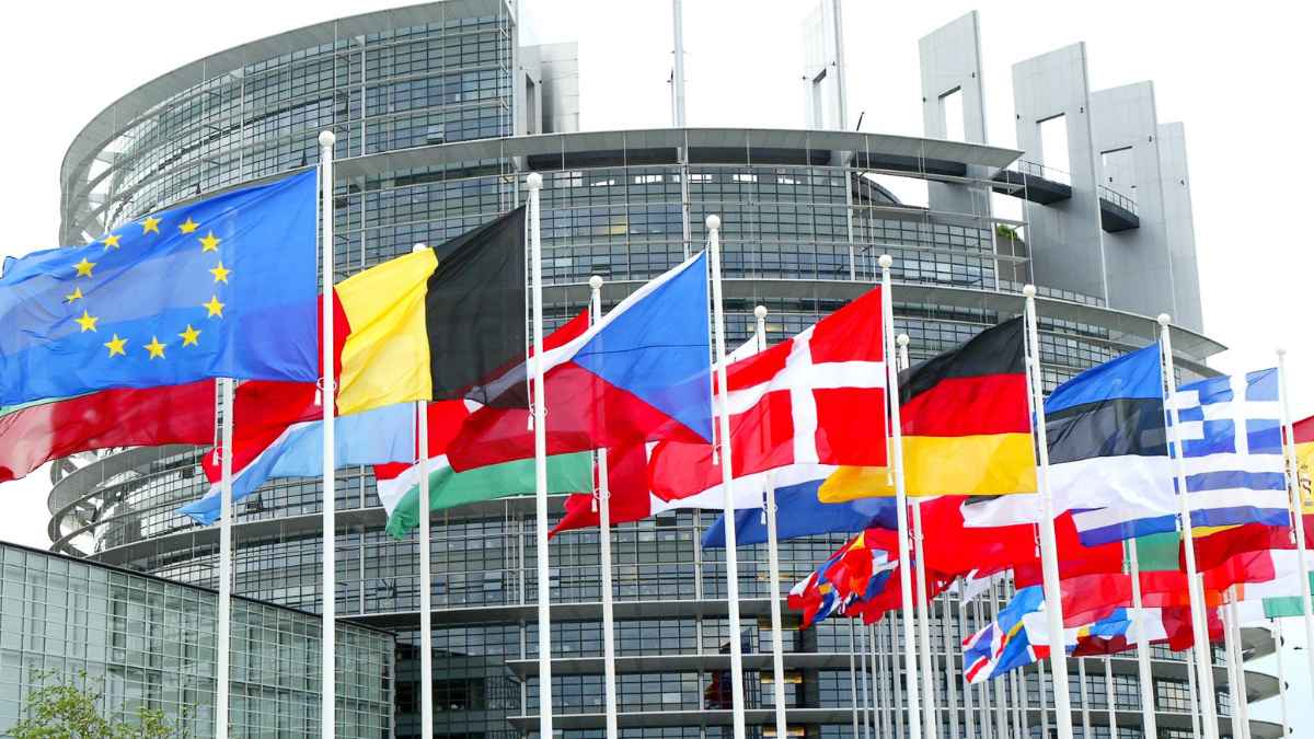 Fachada del Parlamento Europeo con banderas de los países miembros tras aprobar el nuevo impuesto al CO₂ que encarecerá la gasolina y el diésel.