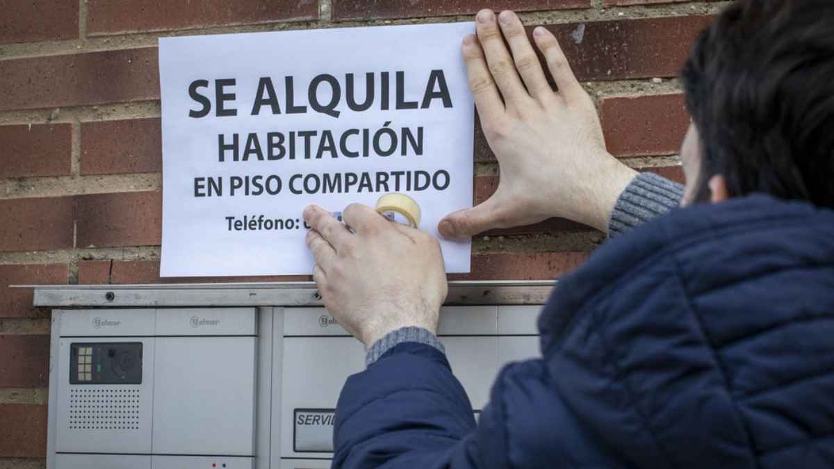 Persona colocando un cartel de se alquila habitación en la fachada de un edificio.