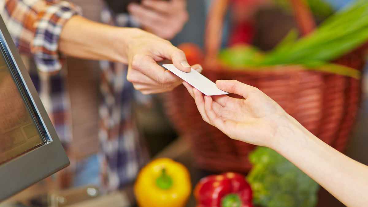Cliente entrega una tarjeta de pago en la caja de un supermercado con frutas y verduras visibles