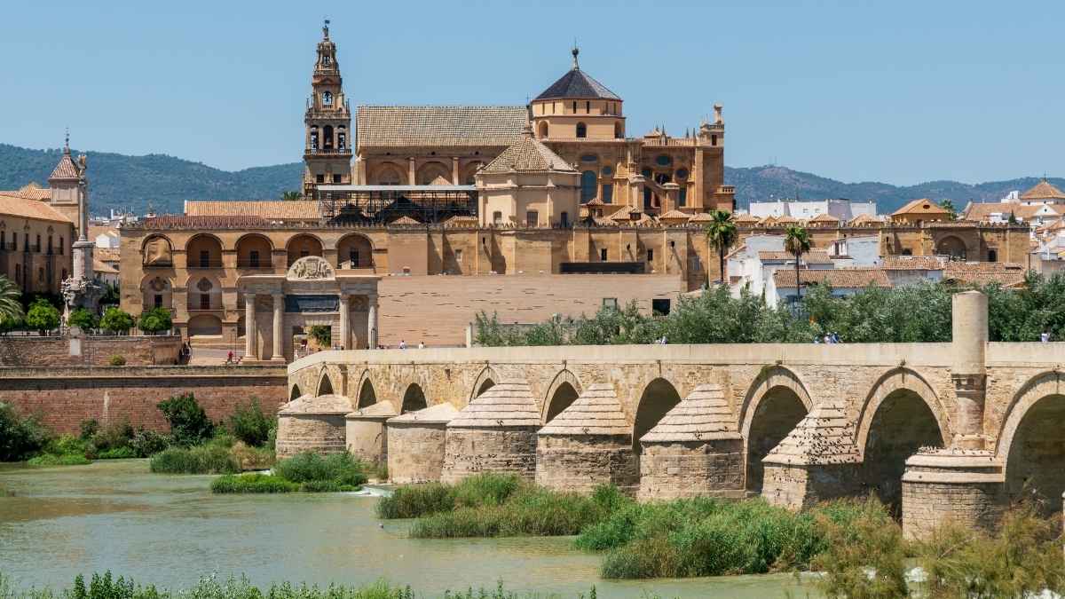 Vista panorámica del Puente Romano y la Mezquita-Catedral de Córdoba sobre el río Guadalquivir en un día soleado.