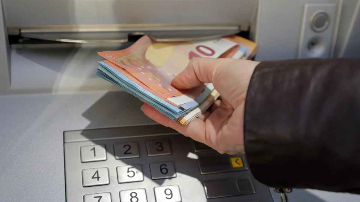 Mano retirando dinero en un cajero automático con billetes de euro.