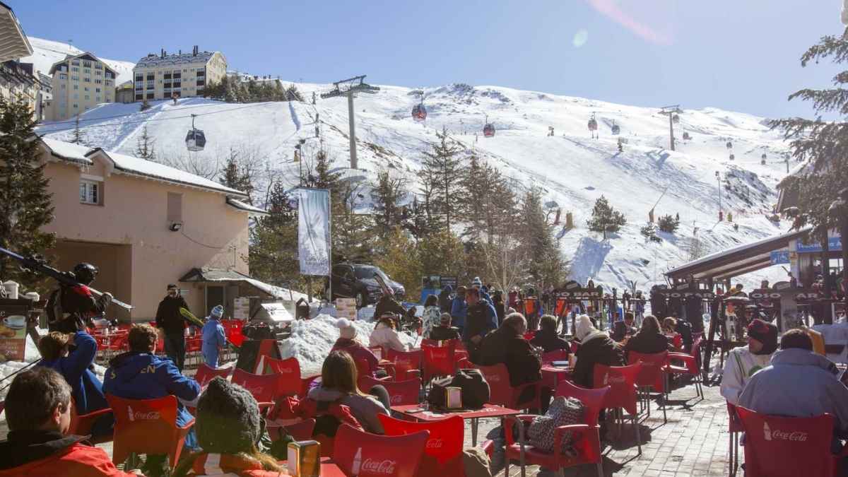 Terraza llena de visitantes en la estación de esquí de Sierra Nevada con telesillas y pistas nevadas al fondo