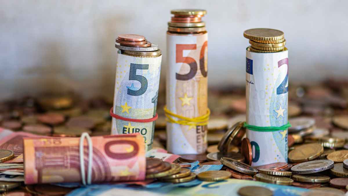 Billetes de euro enrollados con monedas apiladas sobre una mesa llena de cambio