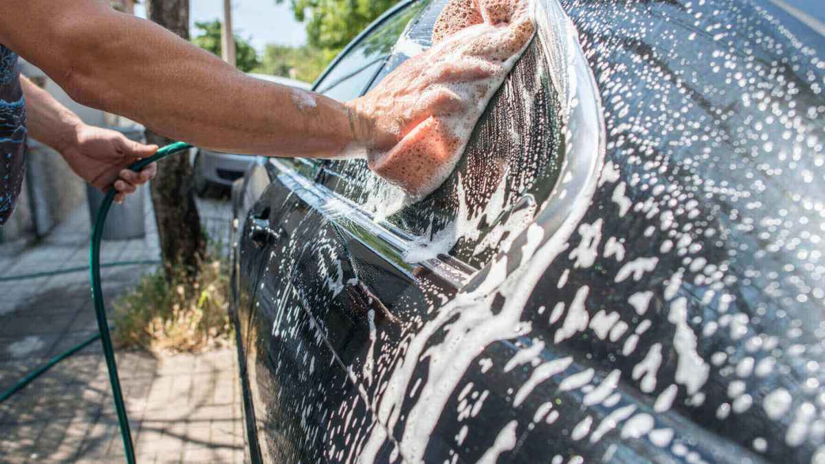Persona limpiando un coche para mantener la matrícula visible y evitar multas de la DGT