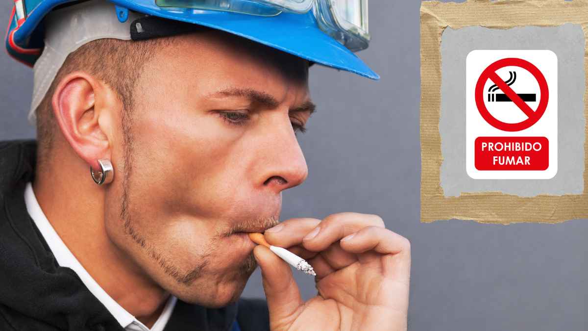 Obrero fumando en su puesto de trabajo junto a un cartel de prohibido fumar durante la jornada laboral