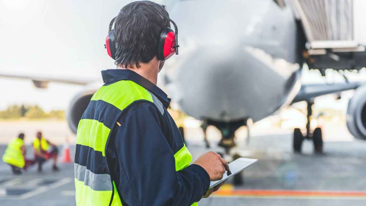 Trabajador de seguridad aeroportuaria realizando tareas en pista junto a un avión