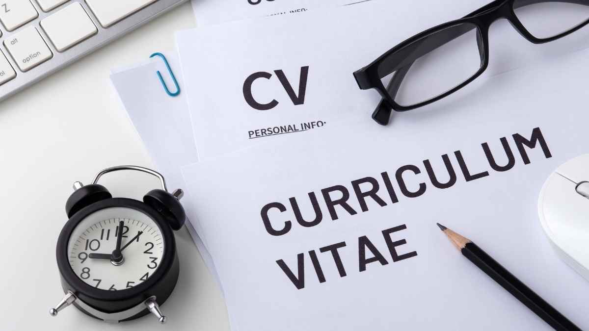 Documentos de curriculum vitae sobre una mesa junto a gafas, reloj y teclado