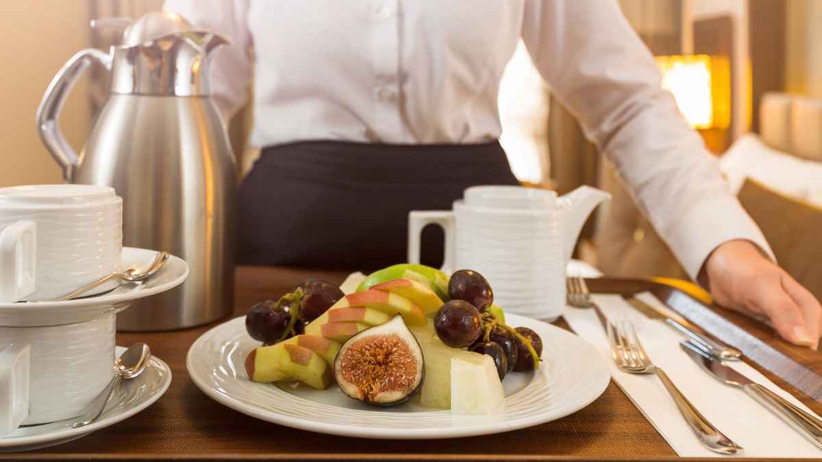 Trabajadora de hotel sirviendo una bandeja de desayuno con fruta y café en una habitación