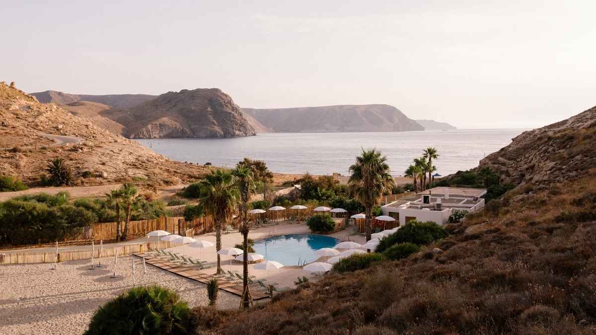 Vista del camping en Cabo de Gata junto al mar, con piscina, palmeras y paisaje natural.