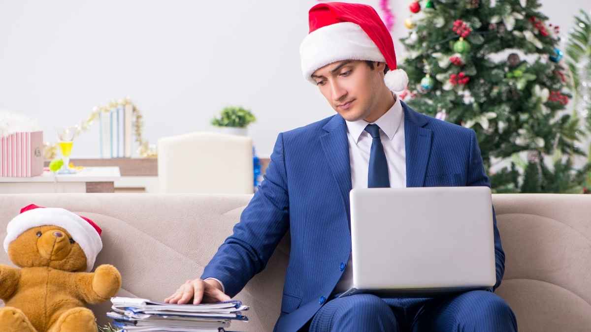 Empleado revisando documentos y trabajando con portátil en Navidad mientras usa un gorro de Papá Noel