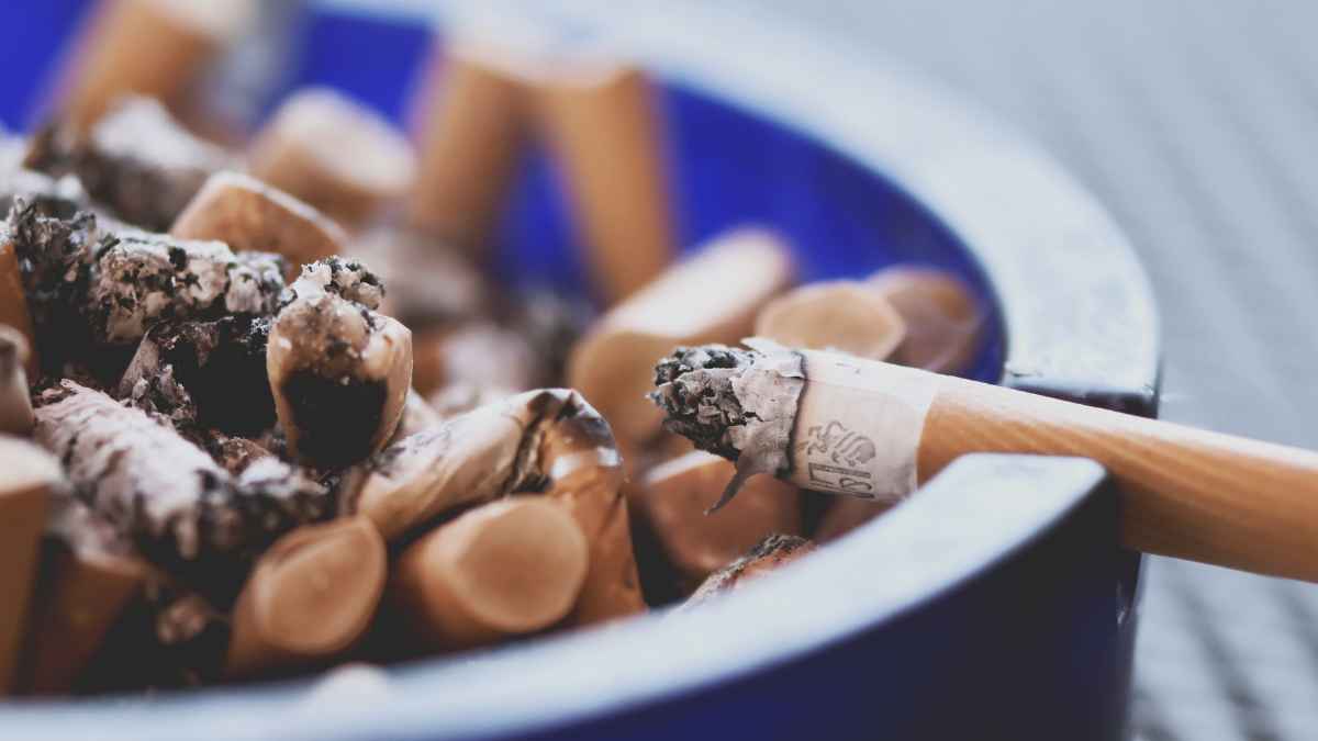 Cenicero lleno de colillas con un cigarrillo encendido que representa el consumo de tabaco tradicional