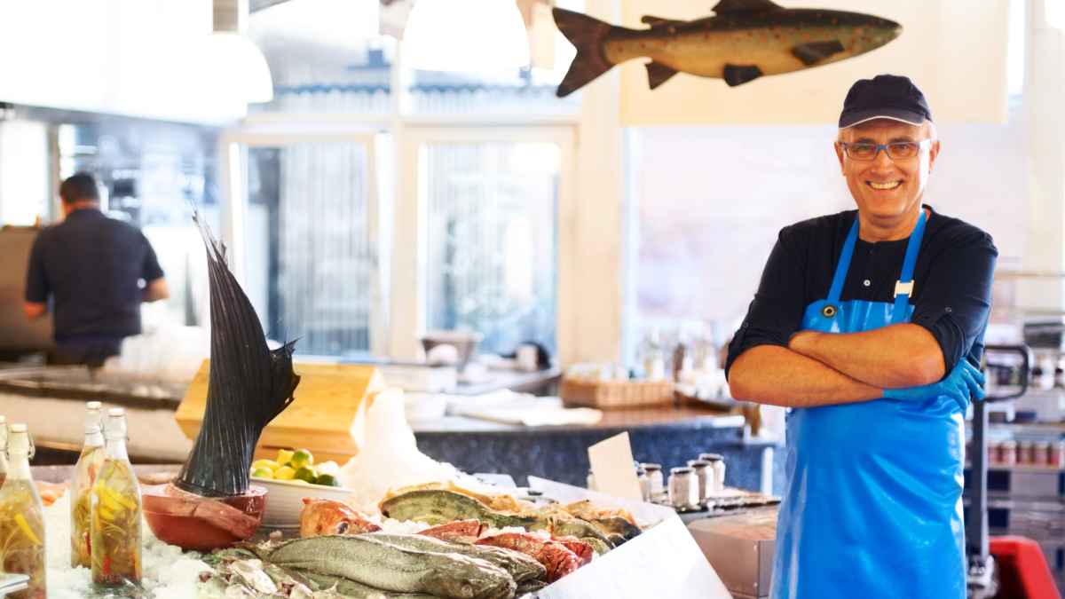 Pescadero sonriente en una pescadería junto a mostrador de pescado fresco